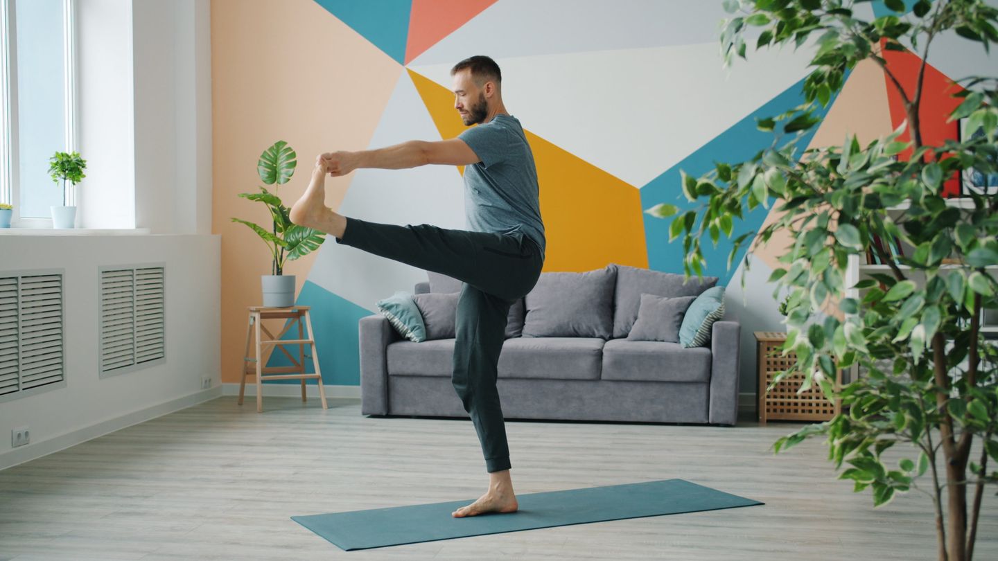 A man performs a yoga pose in a stylish, brightly colored living room. Lifestyle and fitness concept.