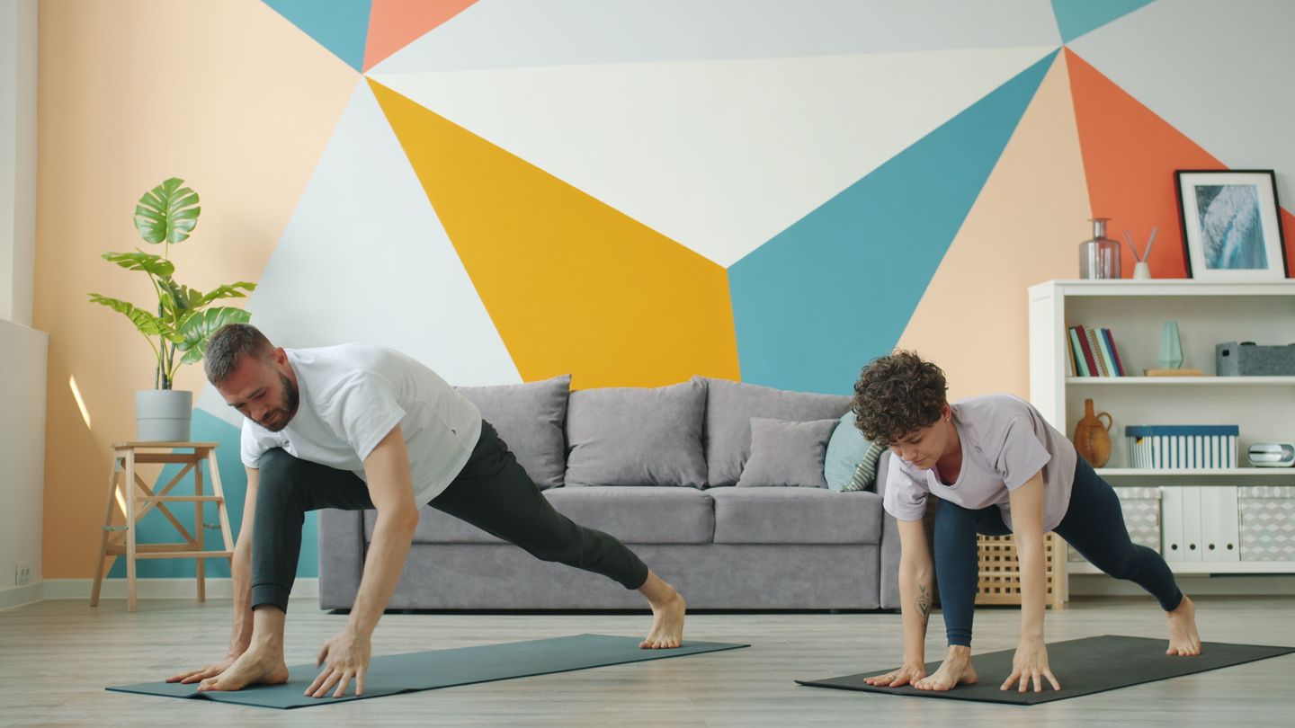 Couple practicing yoga poses in a colorful living room, promoting wellness and relaxation.